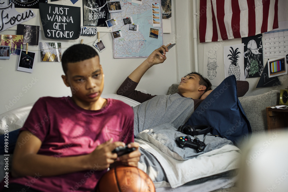 十几岁的男孩在卧室里玩电子游戏和使用智能手机