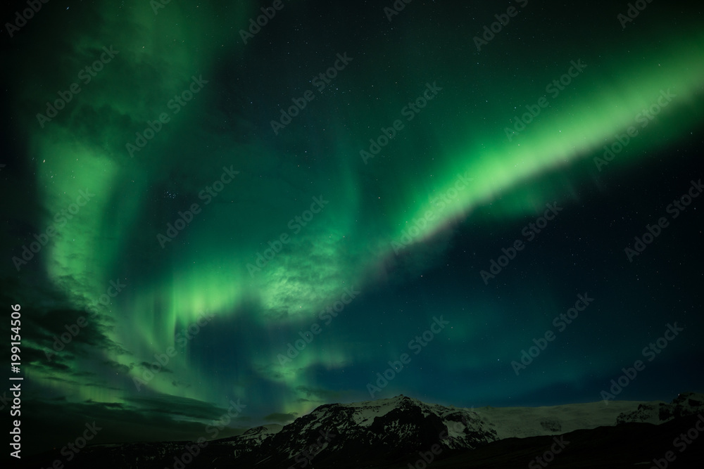 北极光，又名北极光，与冰岛的山脉一起在天空中发光