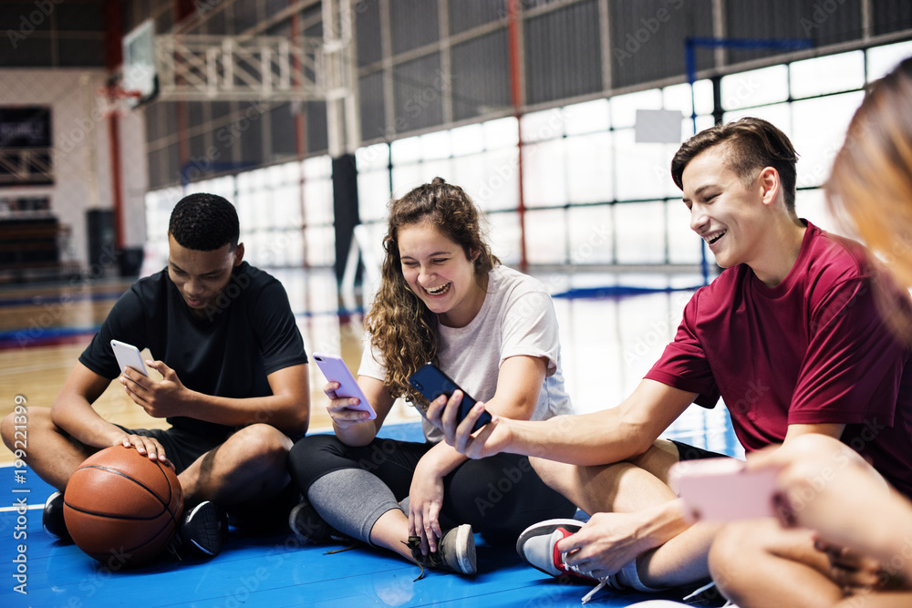一群年轻的青少年朋友在篮球场上放松并使用智能手机