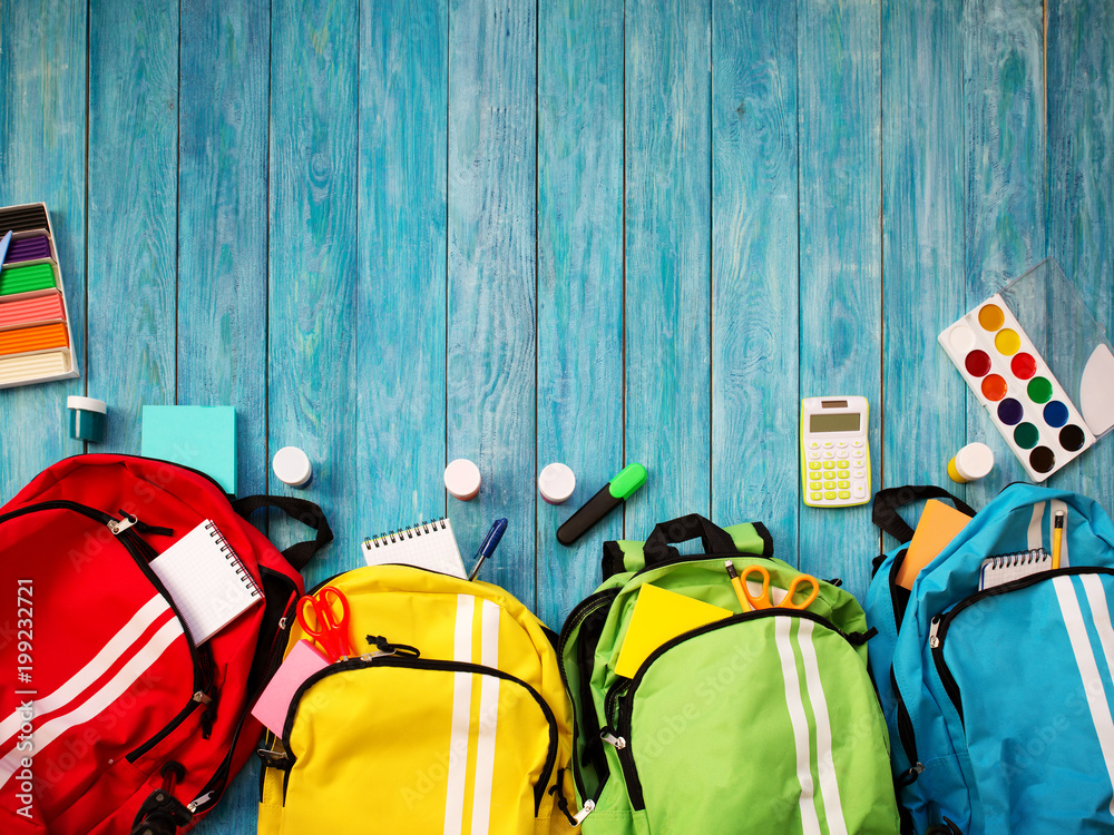 木地板上的彩色儿童书包。带学校配件的背包