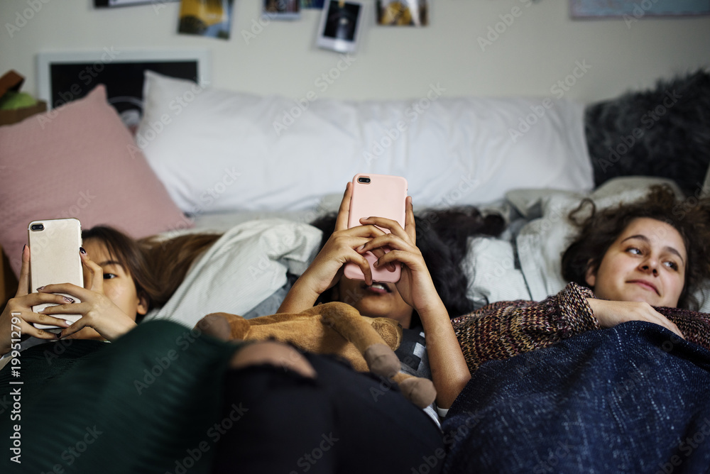 青少年女孩在床上使用智能手机参加睡眠派对