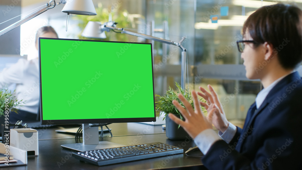 在办公室里，一个商人用实体绿屏在个人电脑上进行视频通话。他在说话