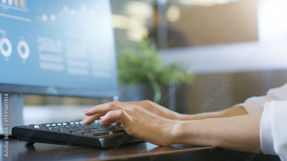 在办公室里，女性用键盘打字，显示器显示带有统计数据的信息图。