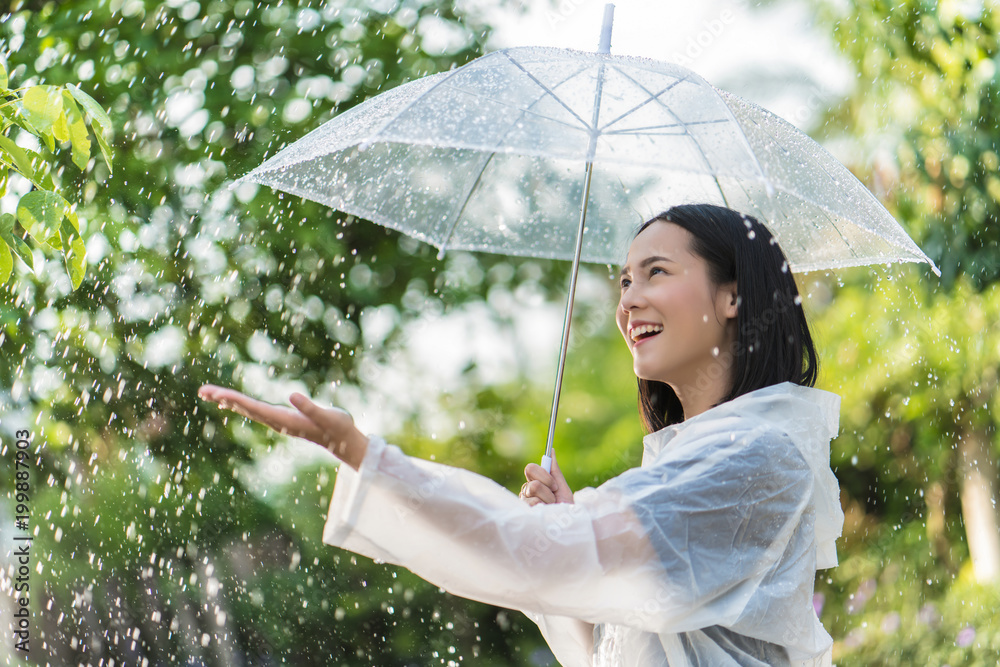 雨天，一个亚洲女人在户外穿着雨衣。她很开心。她用手触摸了雨水。