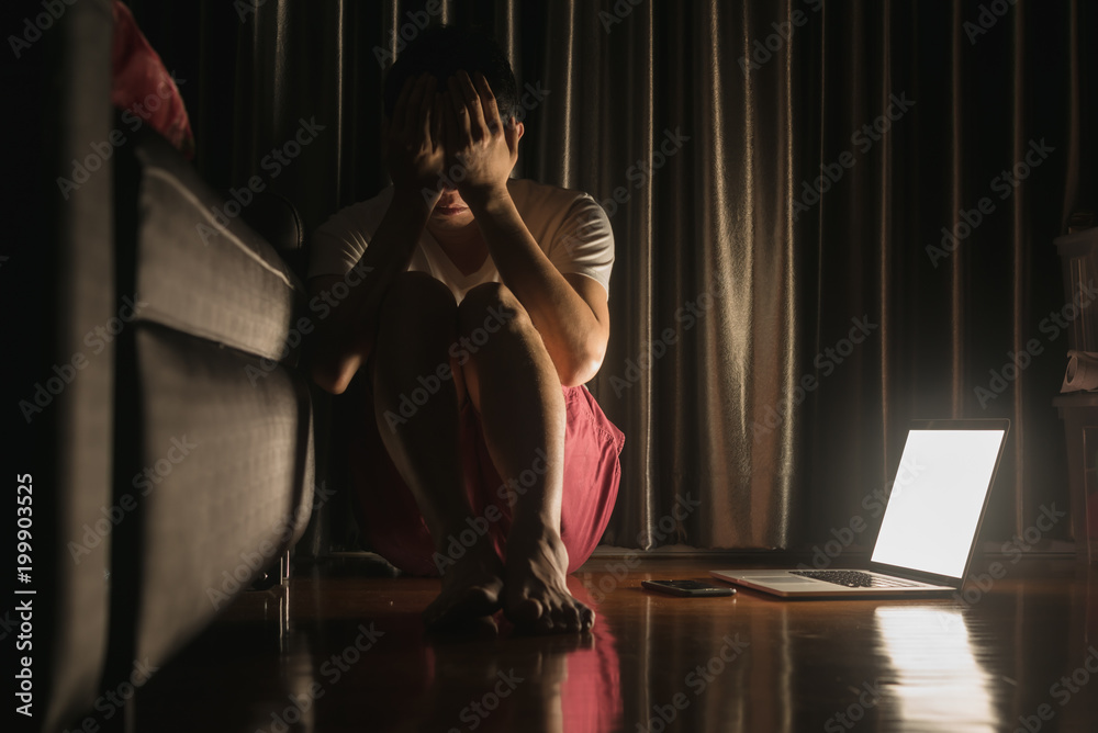 概念图片显示，一名患有抑郁症的男子坐在地板上，旁边放着笔记本电脑和智能手机