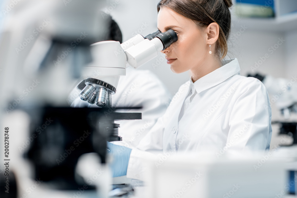 穿着制服的年轻女医生在实验室办公室从事显微镜分析工作