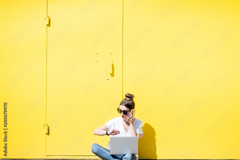 在黄色背景墙上使用笔记本电脑的女人