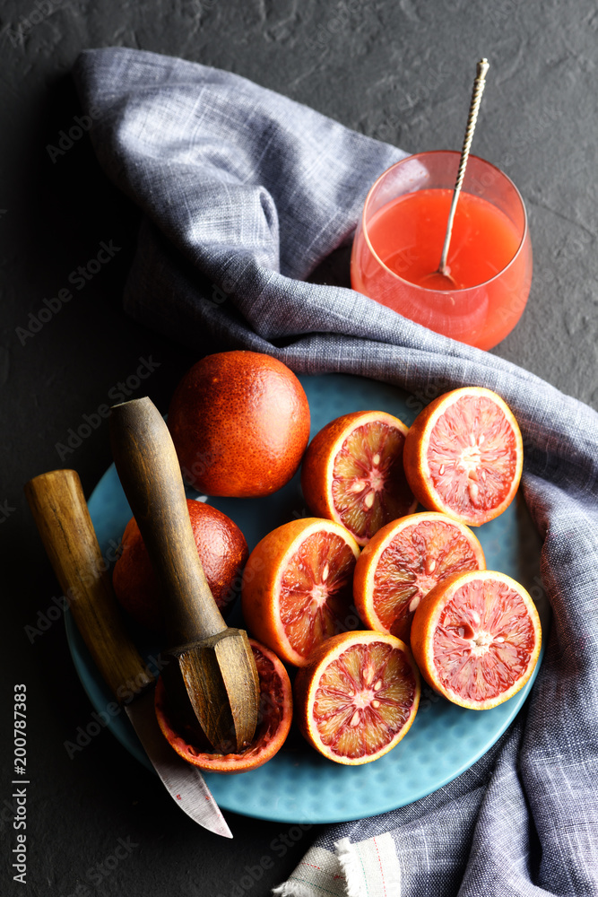 红色西西里橙片和蓝色盘子上的木制挤压器特写。健康饮食维生素概念。