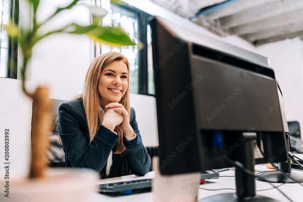 坐在办公室电脑前，笑容满面的女商人。