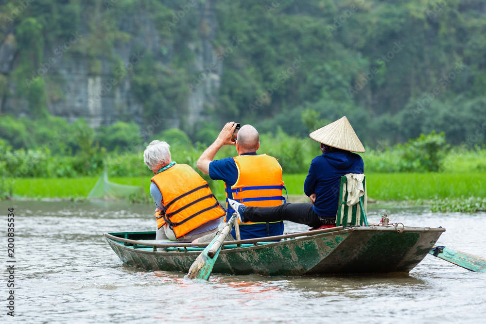 Tourists traveling in boat along the Ngo Dong River and taking picture of the Tam Coc, Rower using f