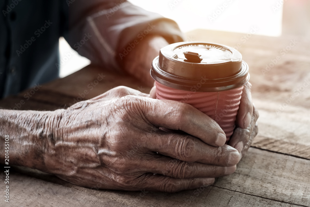 木头桌子上拿着一杯咖啡的老人的手。吸气音