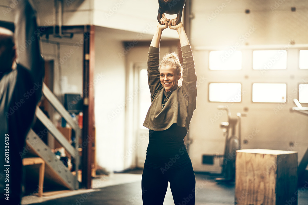 Smiling young woman swinging a weight at the gym