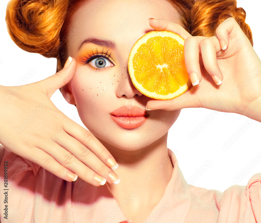 美丽快乐的少女吃多汁的橙子。有雀斑的少女模特，有趣的红色发型，