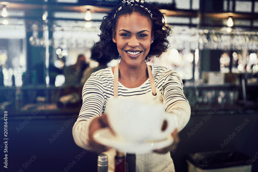 年轻的咖啡师微笑着，手里拿着一杯新鲜的咖啡