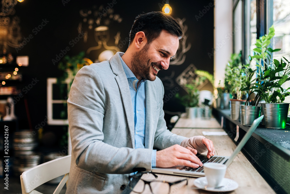 年轻男性，手上裹着绷带，坐在咖啡馆的笔记本电脑前。