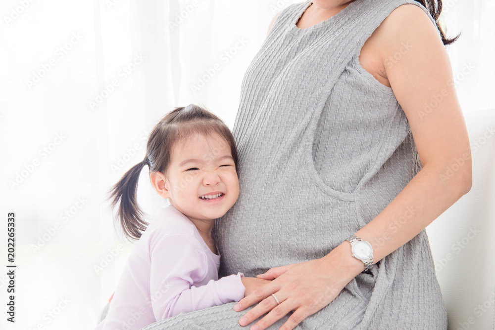 亚洲小女孩听着孕妈妈肚子里传来的声音，面带微笑