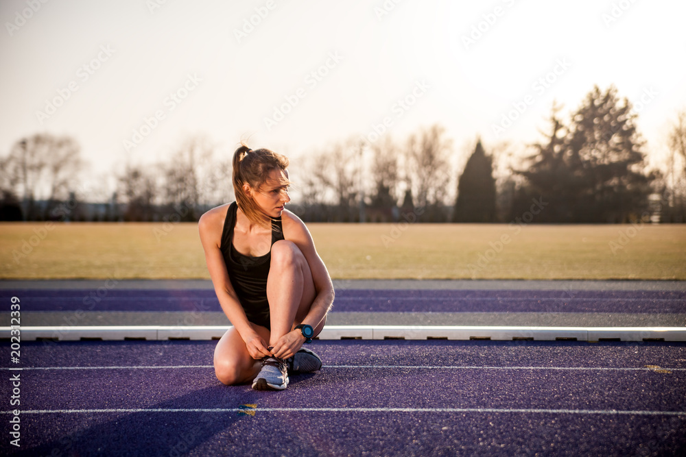 日落时，健身女士在体育场跑道上准备鞋子