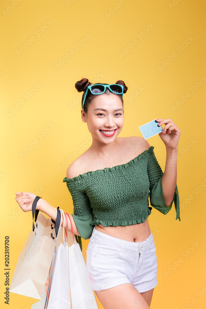 购物的亚洲女人拿着黄色背景的购物袋和信用卡