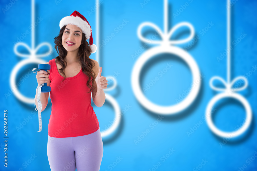 节日合身的黑发女人拿着卷尺和哑铃，在模糊的圣诞背景下