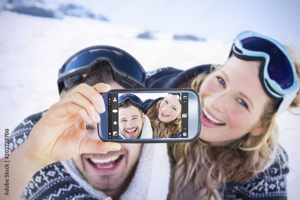 手持智能手机在雪地上与戴着滑雪镜的快乐情侣对抗