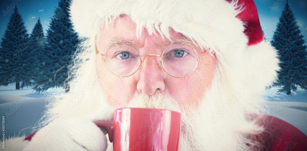 圣诞老人在杉树覆盖的雪地上用红杯子喝水