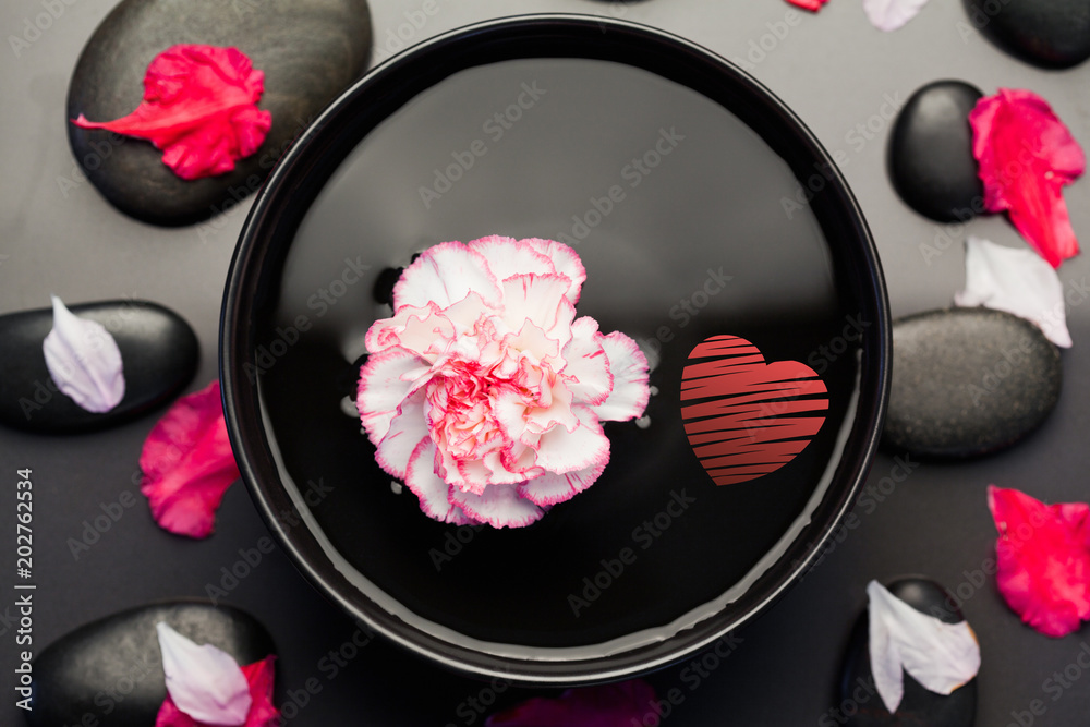 红色的心与漂浮在黑色碗中的白色和粉色康乃馨相映成趣，碗中环绕着黑色的石头和p