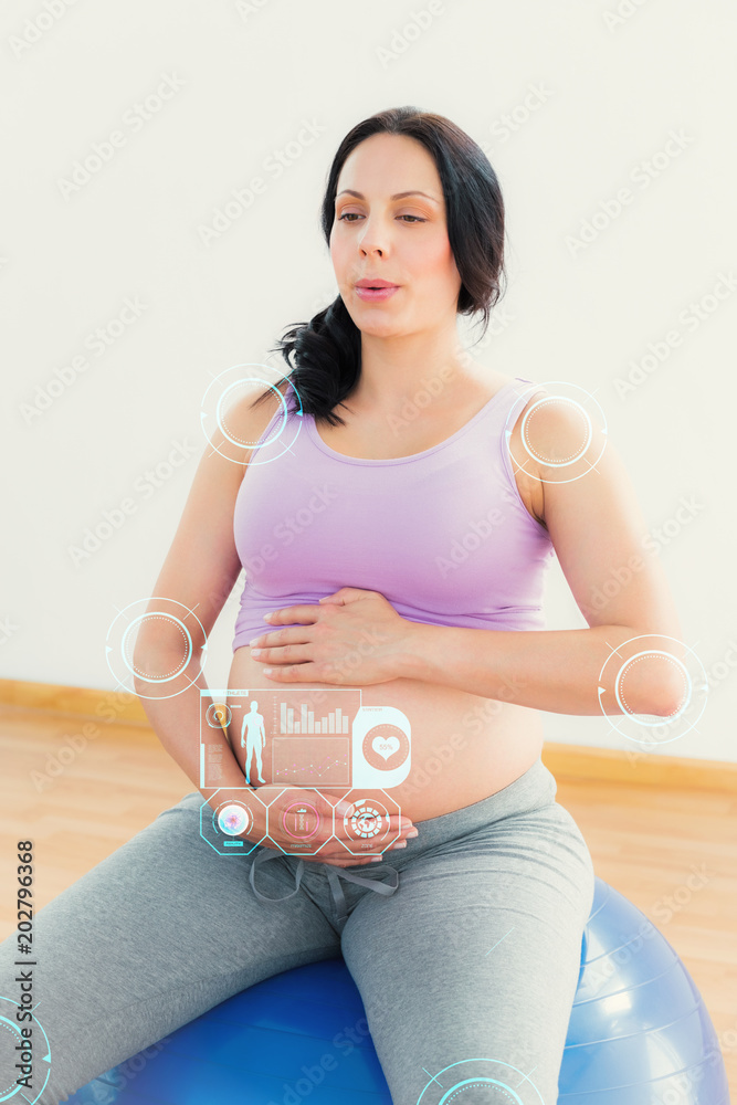 怀孕的深色头发坐在健身球上对着健身界面呼吸