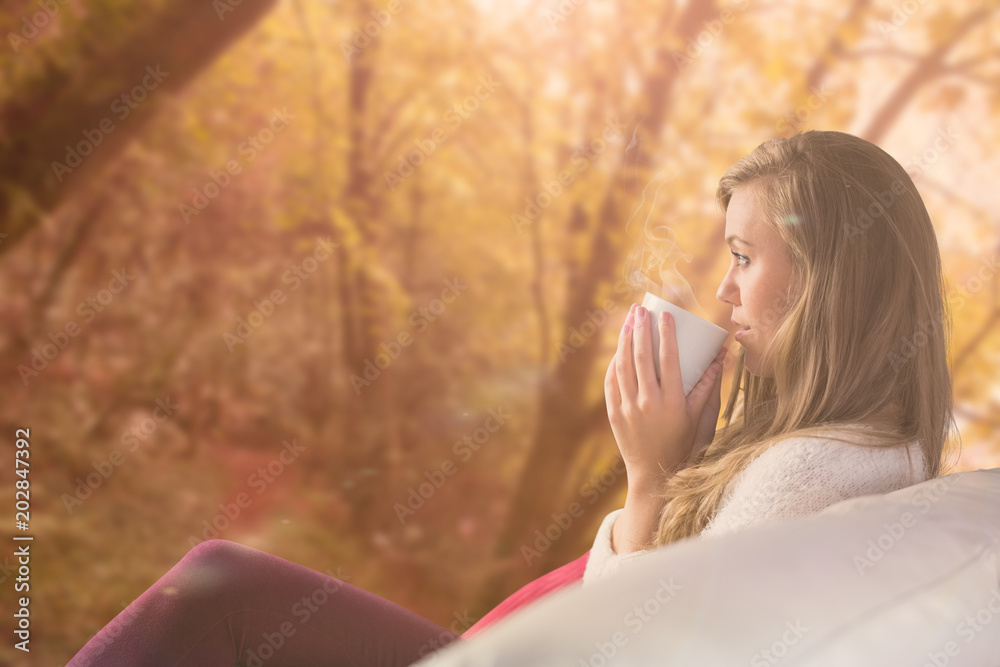 美丽的金发女郎在沙发上喝茶放松，森林中宁静的秋景