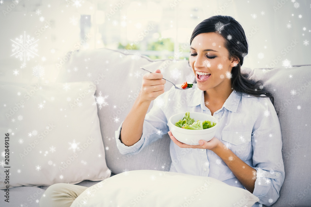 Happy woman relaxing on the sofa eating salad against snow falling