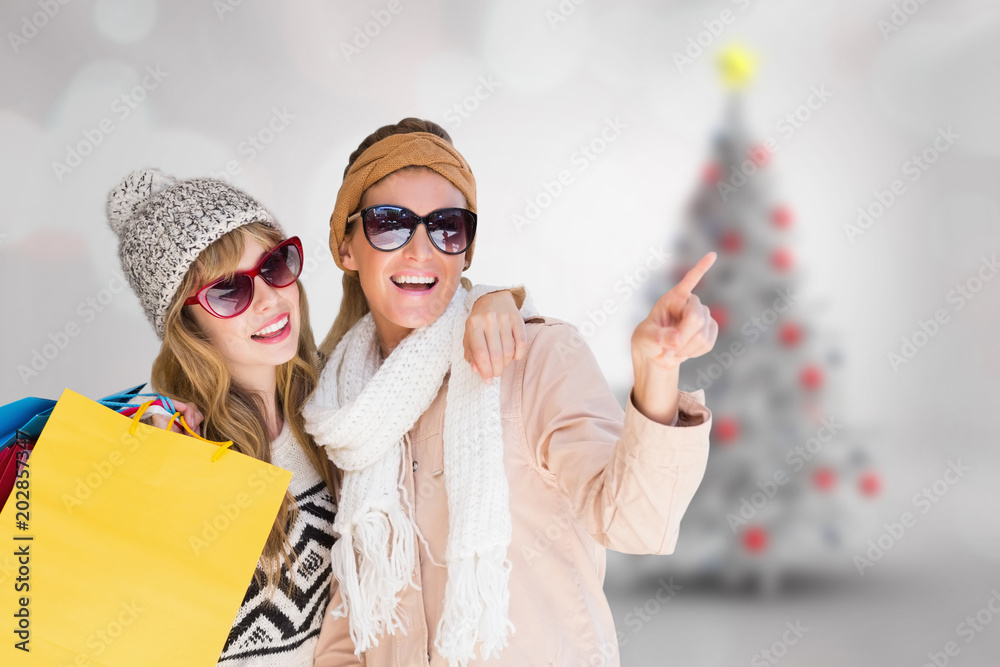 Beautiful women holding shopping bags pointing  against blurry christmas tree in room