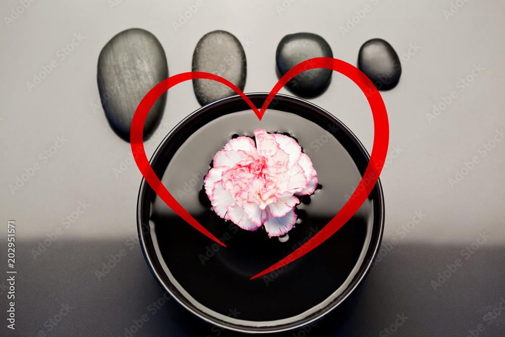 心与漂浮在黑色碗中的粉色和白色康乃馨相映成趣，上面有对齐的黑色鹅卵石