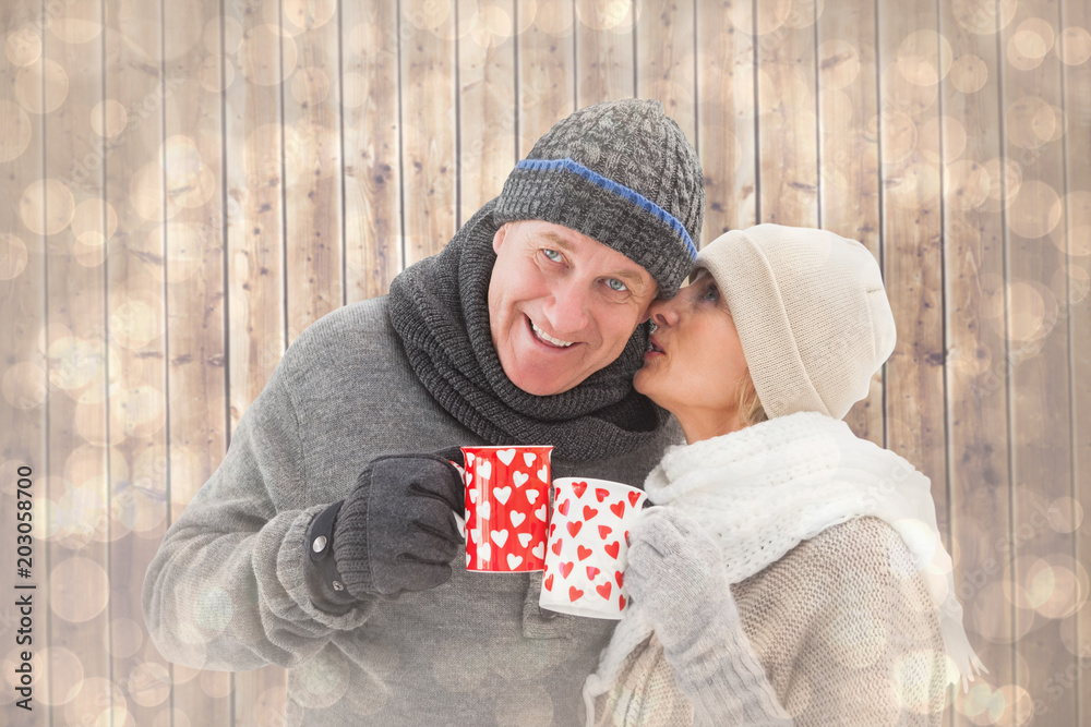 Happy mature couple in winter clothes holding mugs against light glowing dots design pattern