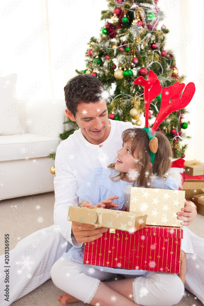 微笑的父亲和女儿在下雪的时候打开圣诞礼物的合成图