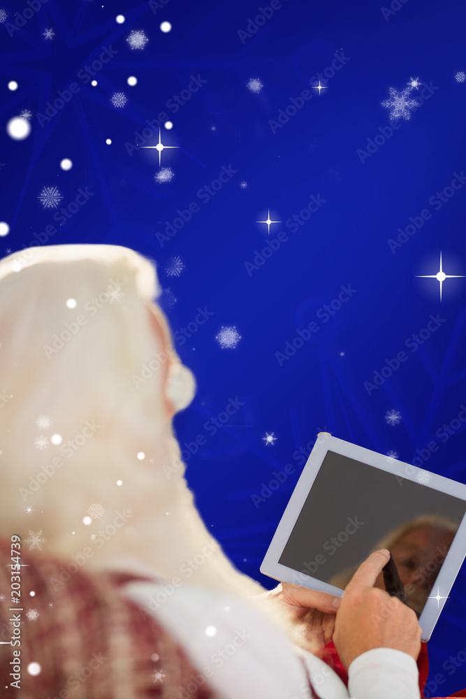蓝色雪花背景下，圣诞老人在扶手椅上使用平板电脑的后视图
