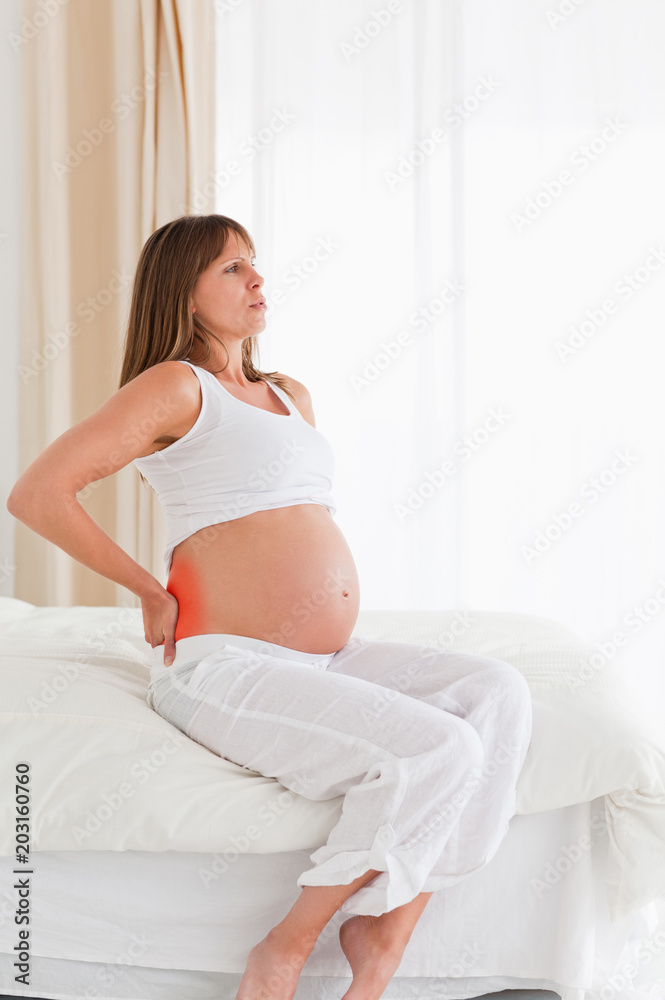 漂亮的孕妇坐在公寓的床上背痛