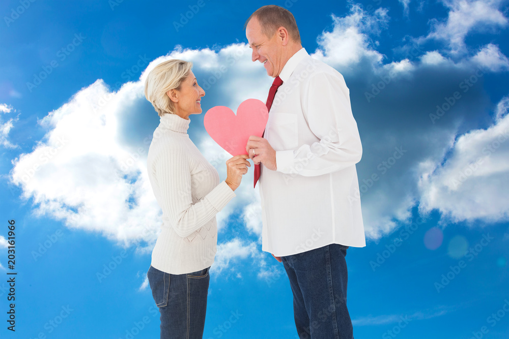 一对年长的深情情侣在多云的天空中抱着粉红色的心形