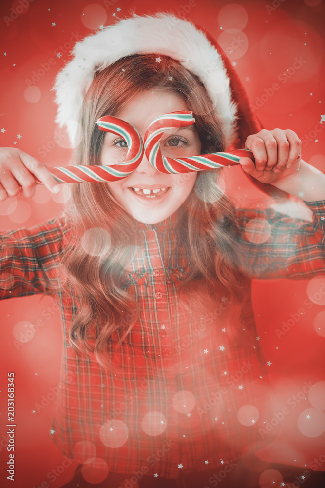 戴着圣诞老人帽的快乐小女孩拿着糖果手杖，对着数字生成的闪烁的灯光