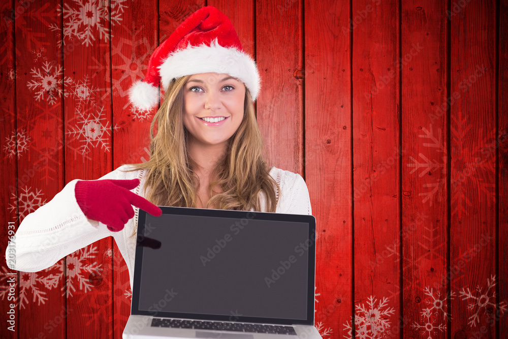 喜庆的金发女郎指着笔记本电脑，对着红色木板上的雪花图案
