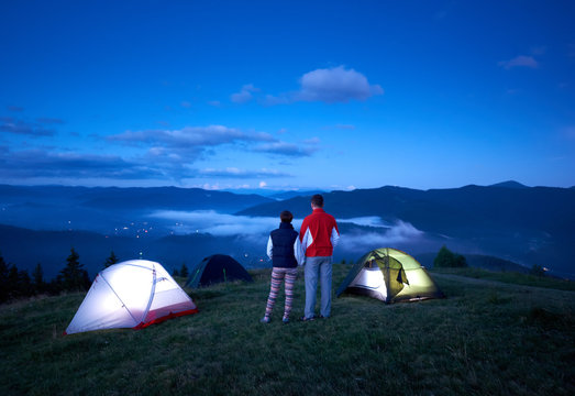 后视图活跃的一对手牵着手在山上露营附近享受日出。雾山和