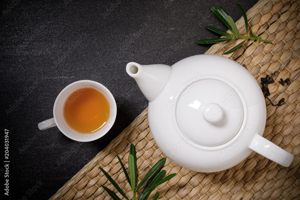 一杯热茶，配蒸壶和干茶，放在黑石桌背景的盘子垫子上w