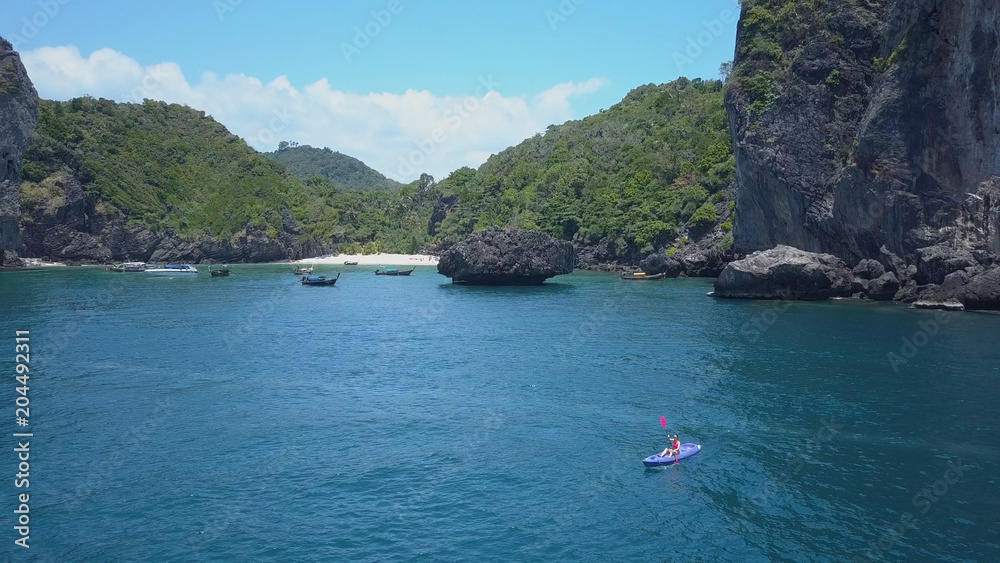 航空：皮划艇上的小女人被巨大的石灰岩悬崖和广阔的大海包围