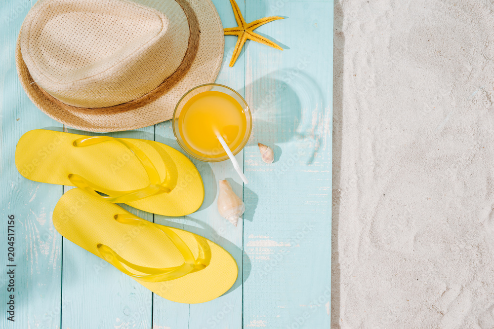 夏日背景。沙滩配饰人字拖、太阳镜、帽子和木制甲板上的橙汁