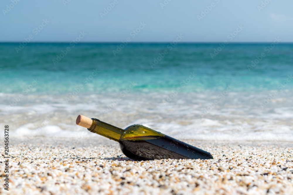 夏日阳光明媚的海滩上的一瓶红酒。背景是大海。