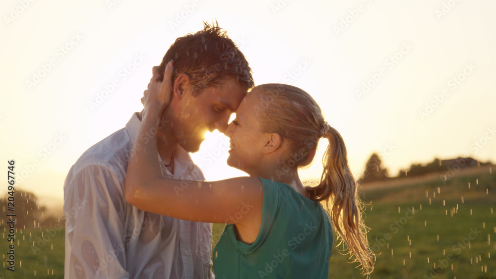 特写：美丽的日落时分，一对可爱的年轻情侣即将在雨中接吻。