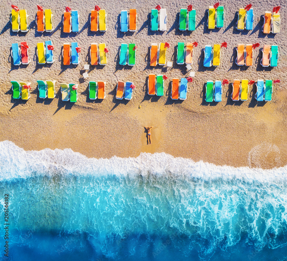 海滩上躺着的女人与彩色躺椅的鸟瞰图。阳光下海上的年轻女人