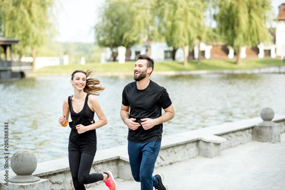 Couple in black sportswear running outdoors near the lake