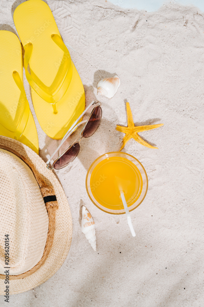 夏日背景。沙滩配饰人字拖、太阳镜、帽子和沙滩背景橙汁