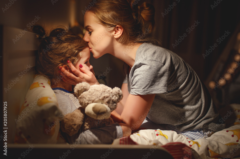 母亲晚上把女儿放在床上亲吻她