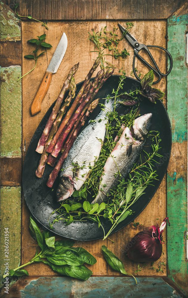 烹饪鱼类晚餐。在质朴的木头上放上未煮熟的生鲈鱼、香草和蔬菜