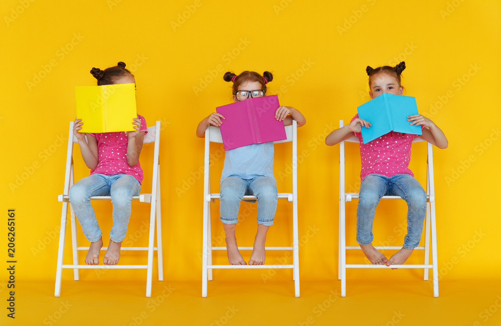 有趣的小女孩在黄色背景上看书。